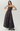 A strapless floor-length gown with a sweetheart neckline, fitted bodice, and full skirt, featuring a dark floral pattern in black and deep burgundy. The model is standing against a light gray studio background.
