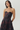 A woman modeling a strapless sweetheart-neckline dress with a dark floral camouflage pattern in black and deep burgundy, featuring a matching waist belt with a rectangular buckle, set against a plain light gray studio background.