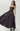 A woman modeling a strapless floor-length gown with a dark floral pattern in deep burgundy and black, set against a plain light gray studio background.
