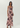A woman modeling a sleeveless, floor-length pink maxi dress with a dark floral print, photographed against a plain light gray studio background.