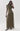 A model wearing a draped olive green maxi dress with a sheer overlay skirt, standing against a plain light gray studio background.