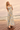 Woman in a floral dress standing on a wooden deck by the ocean.