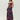 A woman modeling a strapless black maxi dress with a vibrant pink and purple floral print, photographed against a solid light gray studio background.