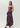 A woman modeling a strapless black maxi dress with a vibrant pink and purple floral print, photographed against a solid light gray studio background.