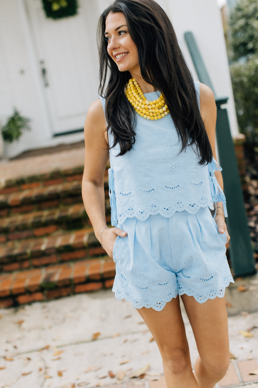 Woman wearing a light blue lace romper with yellow beads in an outdoor setting.