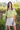 Woman wearing a yellow off-shoulder top and white skirt outdoors.