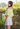 Woman wearing a yellow off-shoulder top and white skirt outdoors.