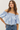 Woman wearing a light blue off-shoulder top and jeans against a plain background