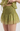 A close-up of a person wearing a light olive green smocked mini skirt with a subtle pink floral pattern, paired with a matching ruffled top.