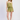 A woman modeling a two-piece olive green romper set with a ruffled smocked top and matching shorts, paired with beige woven flat shoes, against a light gray studio background.