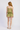 A woman viewed from the back wearing a light olive green two-piece set consisting of a ruffled camisole top and matching shorts, paired with woven tan sandals, against a plain white studio background.