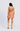 Woman wearing an orange patterned dress with cut-out back and beige cowboy boots on a white background