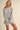 A woman modeling an oversized light gray knit sweater with matching ribbed shorts against a plain beige studio background.