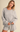 A woman wearing a light heather gray knit crewneck sweatshirt and matching shorts, standing against a plain beige studio background.