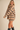A woman modeling an oversized beige knit sweater with horizontal black stripes, featuring a high ribbed turtleneck and long sleeves, paired with black boots against a solid beige background.