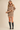 A woman models an oversized beige and black striped knit sweater dress with a ribbed cowl neck, long sleeves, and a ribbed hem, styled with black knee-high boots against a solid beige background.