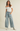 Woman wearing a white off-shoulder top and studded blue jeans on a beige background