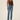A model wearing a brown ribbed tank top and light blue straight-leg jeans, standing against a plain beige studio background.