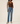 A model wearing a brown ribbed tank top and light blue straight-leg jeans, standing against a plain beige studio background.