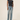 A model wearing a dark charcoal gray short-sleeve crewneck t-shirt and light-wash blue straight-leg jeans, paired with burgundy flat shoes, against a plain beige studio background.
