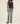 A model wearing a dark charcoal gray short-sleeve crewneck t-shirt and light-wash blue straight-leg jeans, paired with burgundy flat shoes, against a plain beige studio background.