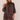 A woman modeling a dark brown tiered ruffle mini dress with a high mock neck and sheer long sleeves, set against a plain light beige background.