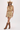 A woman modeling a sleeveless cream-colored mini dress with a vintage floral pattern, styled with a straw cowboy hat and brown leather cowboy boots against a plain white studio background.