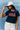 Woman wearing a navy t-shirt with 'USA' text, white cap, and light pants against a blue textured background