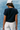 Person wearing a navy blue t-shirt and light-colored pants against a textured blue wall.