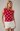 Woman wearing a red polka dot top and white shorts against a plain background