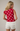 Woman wearing a red polka dot top and white shorts against a plain background