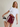 A woman modeling a white cropped t-shirt and burgundy athletic shorts with white side stripes, holding up a black and white striped athletic sock against a plain beige studio background.