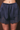 A close-up of a person wearing navy blue satin shorts with a gathered elastic waistband and dark lace trim at the hem, shown against a dark brown background.