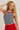 Young woman wearing a striped tank top and red pants against a plain background
