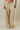 A person wearing loose, wide-leg drawstring pants with horizontal yellow and dark gray stripes, paired with white slide sandals, against a plain beige studio background.