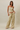 A woman modeling a matching two-piece lounge set with a strapless tube top and wide-leg drawstring pants, both in a beige and olive green striped pattern, against a solid beige studio background.