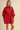 A woman modeling a bright red long-sleeve shirt dress with a matching tie belt, photographed against a plain beige studio background.