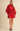 A woman modeling a bright red long-sleeve shirt dress with balloon sleeves, a button front, and a matching waist tie, paired with black Mary Jane heels against a solid beige studio background.