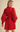 A woman wearing a bright red mini dress with balloon sleeves and a matching waist tie, shown from the back against a plain beige studio background.