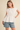Woman wearing a white blouse and denim shorts on a beige background