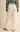 A person shown from the back wearing cream wide-leg pants, a green patterned sweater, and gray sneakers against a plain beige studio background.