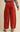 A person shown from the back wearing rust-red wide-leg corduroy pants, a multicolor knit sweater, gray socks, and brown wedge sandals against a plain beige studio background.