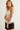 A woman modeling a sleeveless white tank top paired with black denim shorts against a plain light gray studio background.