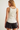 A woman shown from the back wearing a cream-colored ribbed tank top with beige trim and black denim shorts against a plain light background.