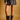 A model from the waist down wears a dark brown faux-leather mini skirt with front buttons and dark brown mid-calf boots with buckle straps, set against a solid warm tan studio background.