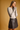 A woman posing in a light beige long-sleeve knit top and a black faux-leather mini skirt against a solid warm tan background.