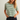A woman modeling a short-sleeve crewneck t-shirt with green and off-white horizontal stripes, paired with dark denim shorts, against a plain light gray background.
