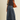 A woman modeling a dark brown short-sleeve mock neck top and a high-waisted blue denim midi skirt, carrying a large brown suede shoulder bag against a solid light beige background.