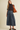 A woman modeling a dark brown short-sleeve mock neck top and a high-waisted blue denim midi skirt, carrying a large brown suede shoulder bag against a solid light beige background.
