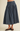 A dark blue denim midi skirt with a gathered waist and pleated skirt, shown on a model wearing brown suede flats against a light beige background.